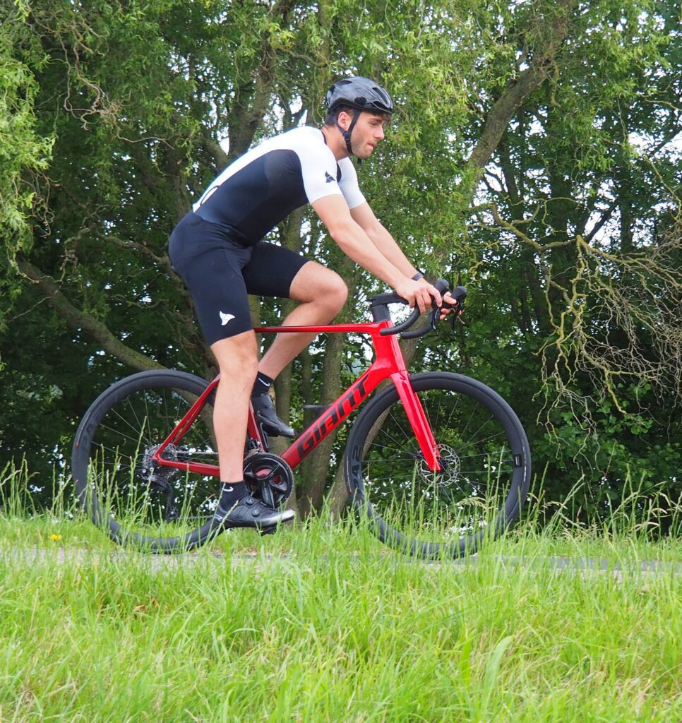 Coach in actie tijdens hybride coaching – fietsend op de dijk in rood trisuit